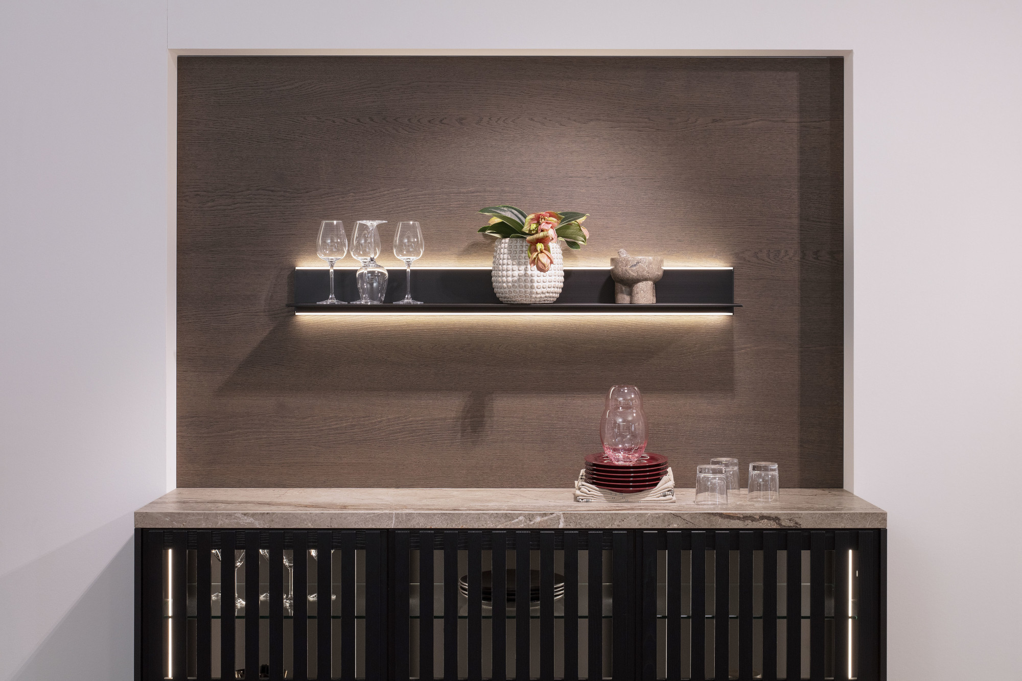 Marmorierte Anrichte mit Gläsern, Karaffe und beleuchtetem Regal mit Vase und Gläsern.