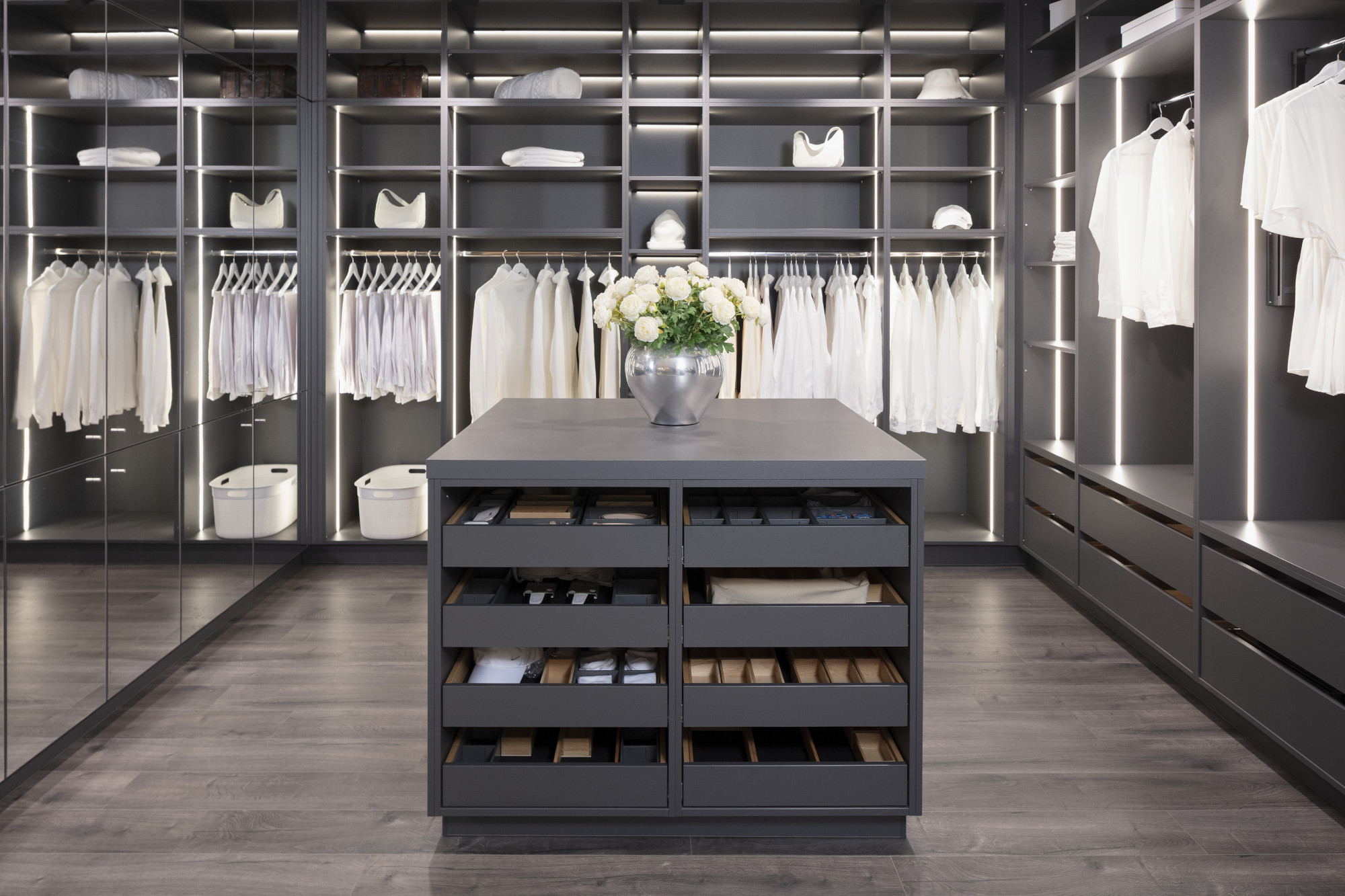 Moderner, geordneter begehbarer Kleiderschrank mit weißen Hemden und Blumenstrauß auf Kommode.