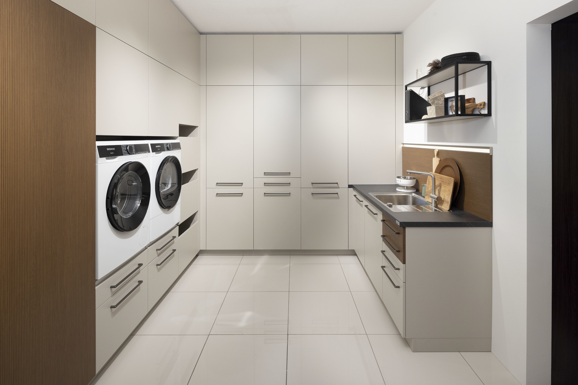 Moderne Waschküche mit Waschmaschine, Trockner und Einbauschränken in neutralen Farben.