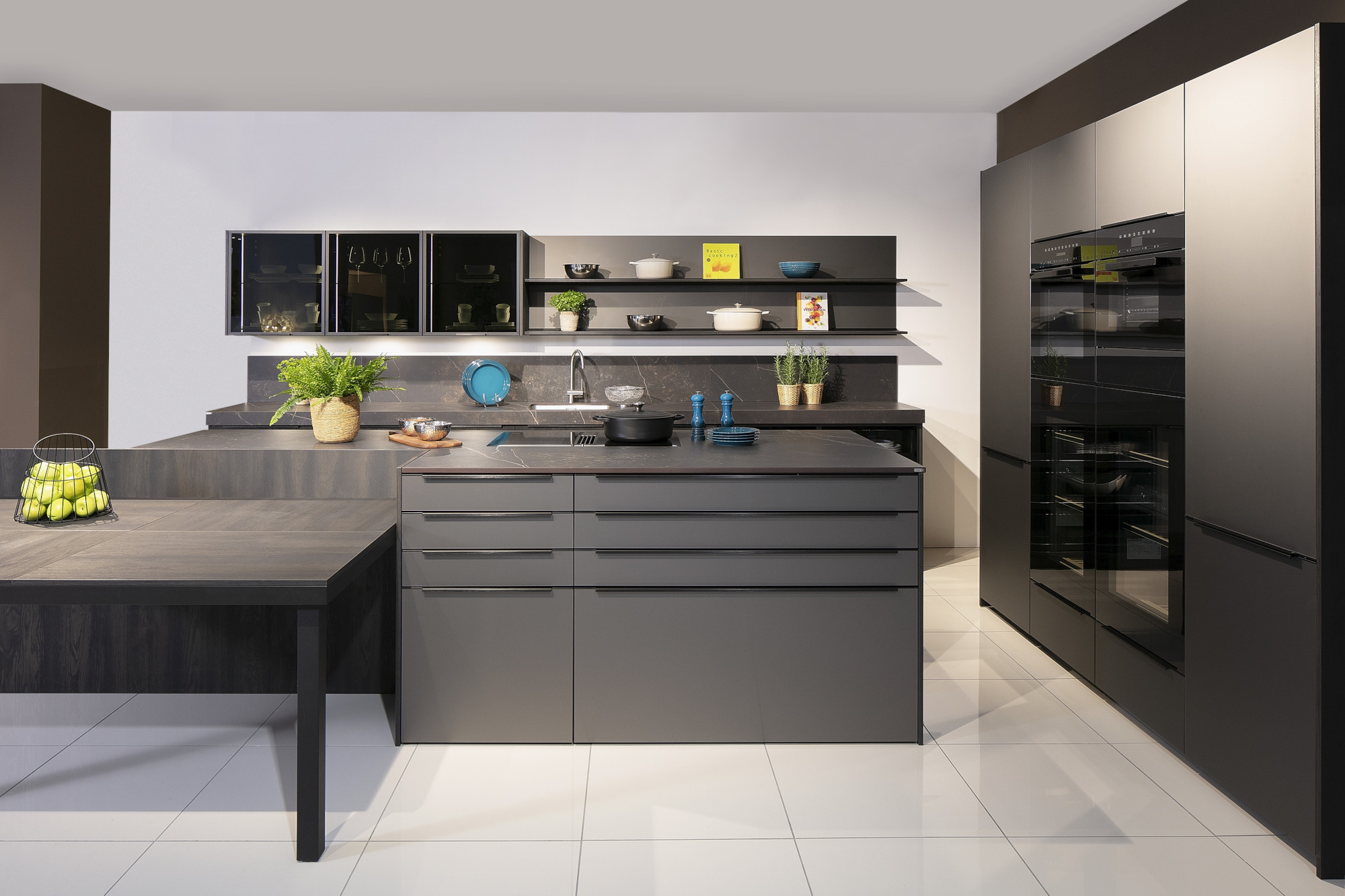 Moderne schwarze Küche mit Kochinsel, offenen Regalen und grünen Pflanzen.