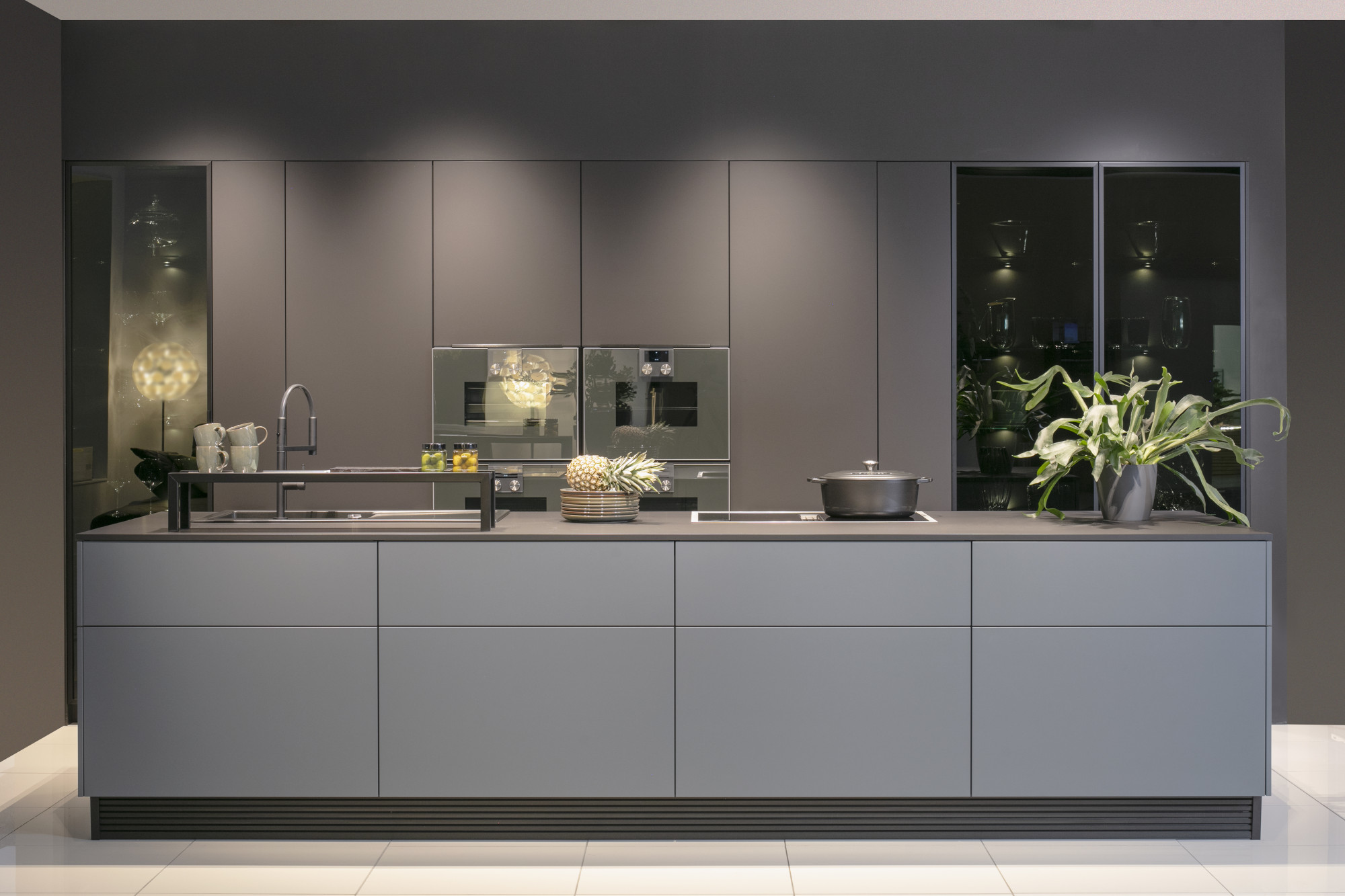 Moderne graue Küche mit Kochinsel, Pflanzen und dezentem Licht.