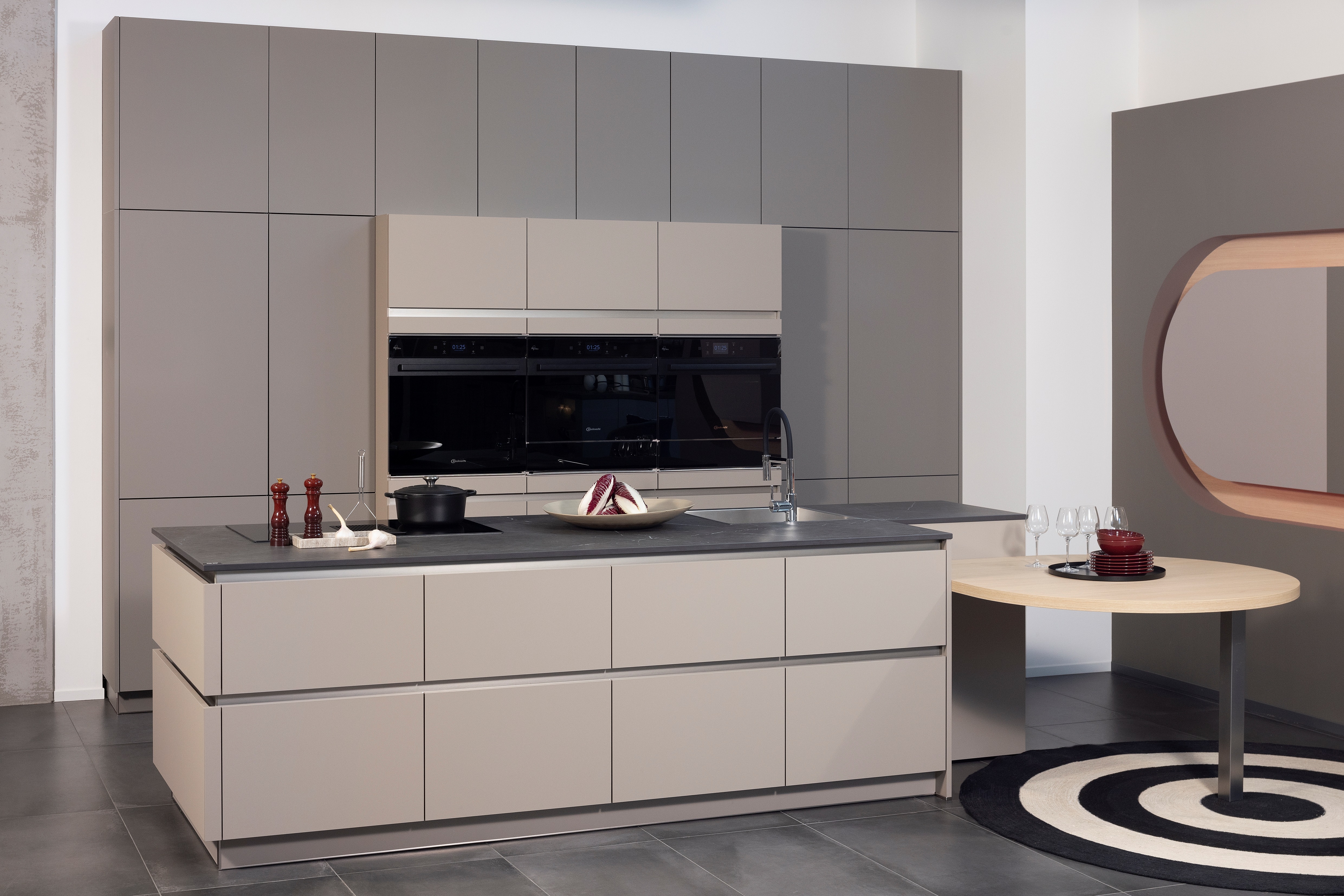 APL:Keramik Front: FEEL Farbe Basalt Front: FEEL FArbe Taupe Korpus: Graphit Griff: Grifflos Griffleiste Edelstahl Geräte: Bauknecht Armatur: Franke Spüle: Franke  Features: Keramik-APL, architektonisch stringente Planung, exakte Linienführung, Hochschränke teil eingekoffert, erzeugt verschiedene Tiefenwirkungen.