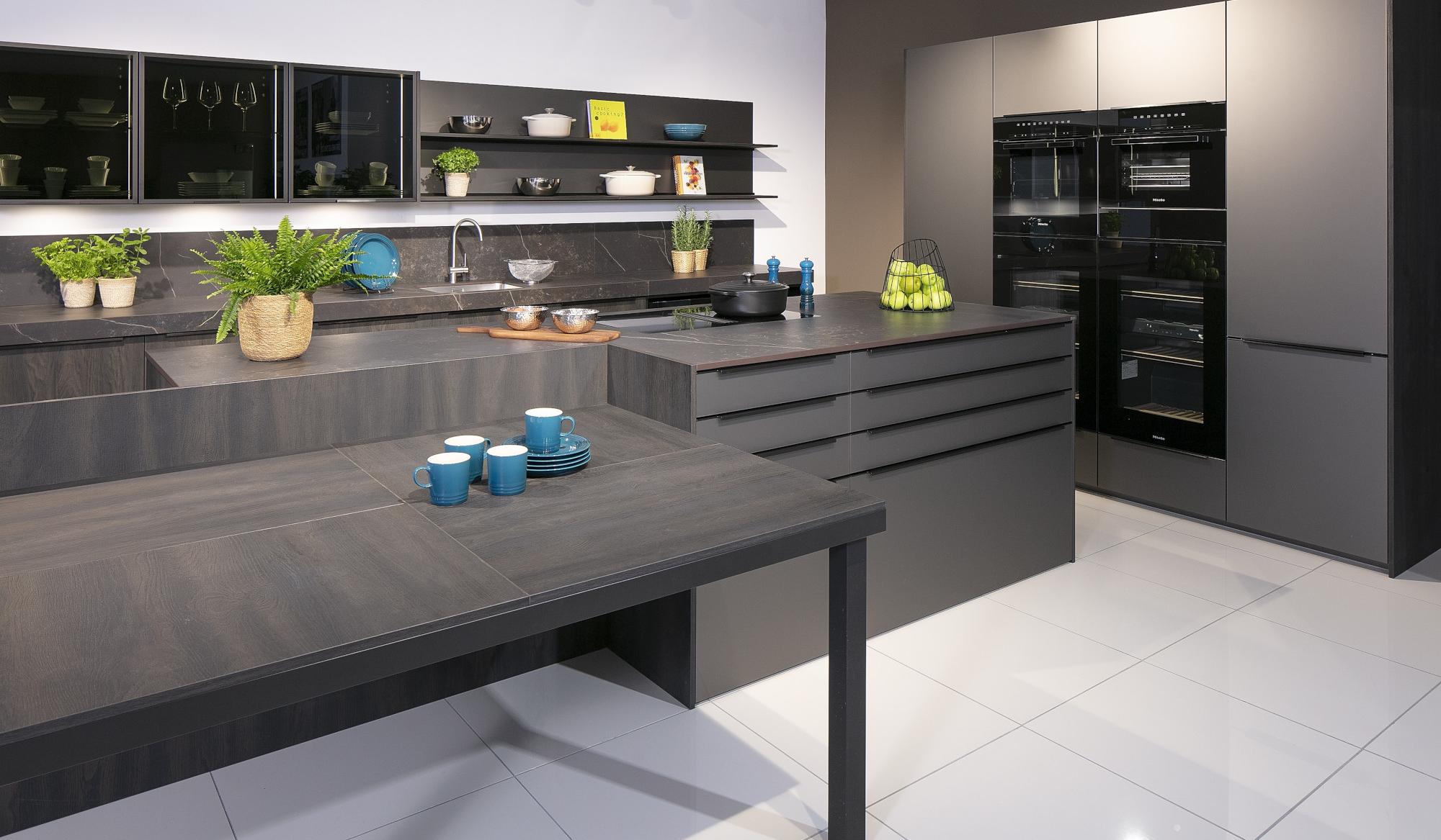 Moderne Küche mit dunklen Schränken, weißem Boden, Pflanzen und Tassen auf dem Tisch