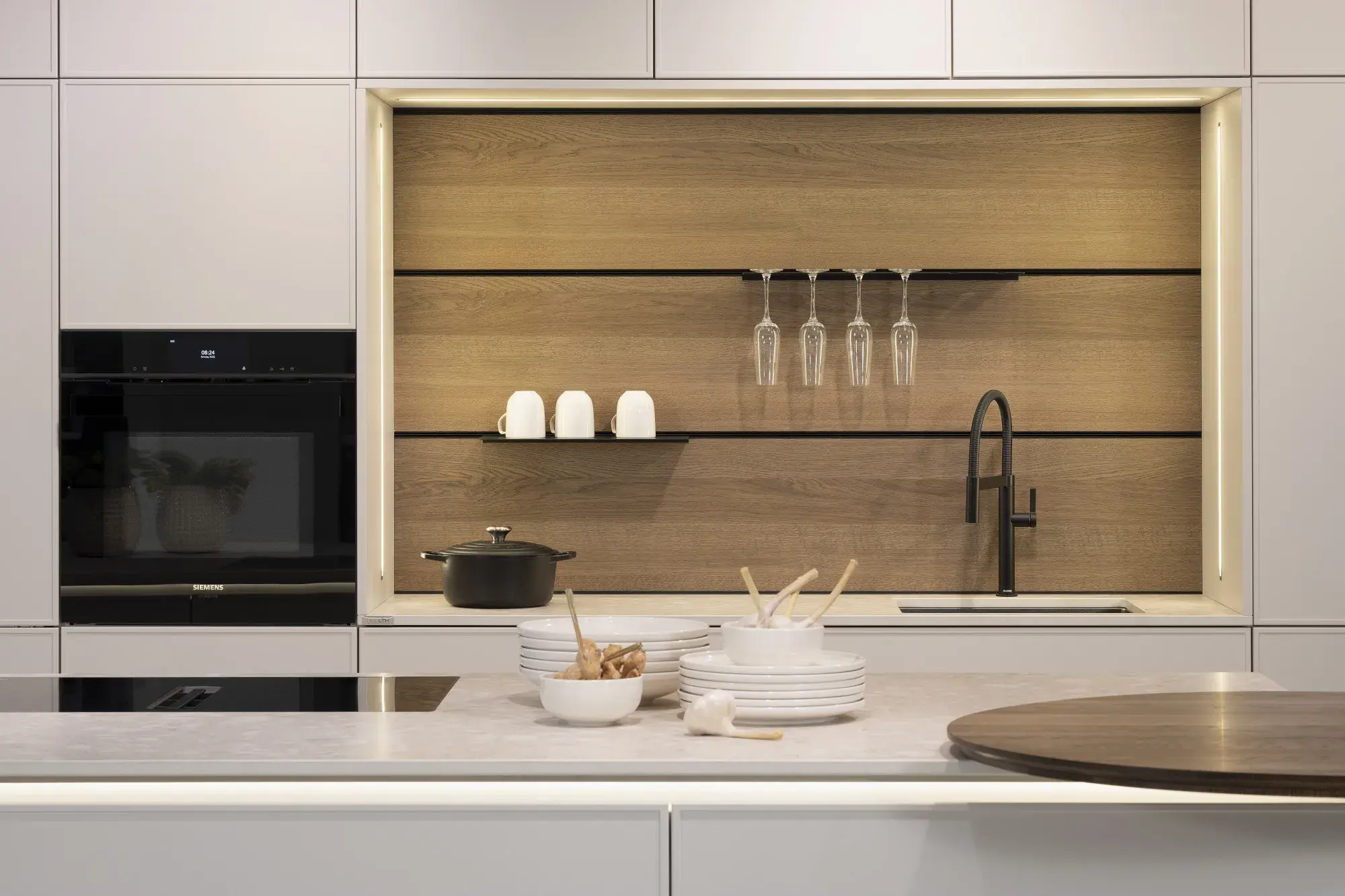 Moderne Küche mit heller Arbeitsplatte, Geschirr und Holzrückwand, schwarzer Wasserhahn.