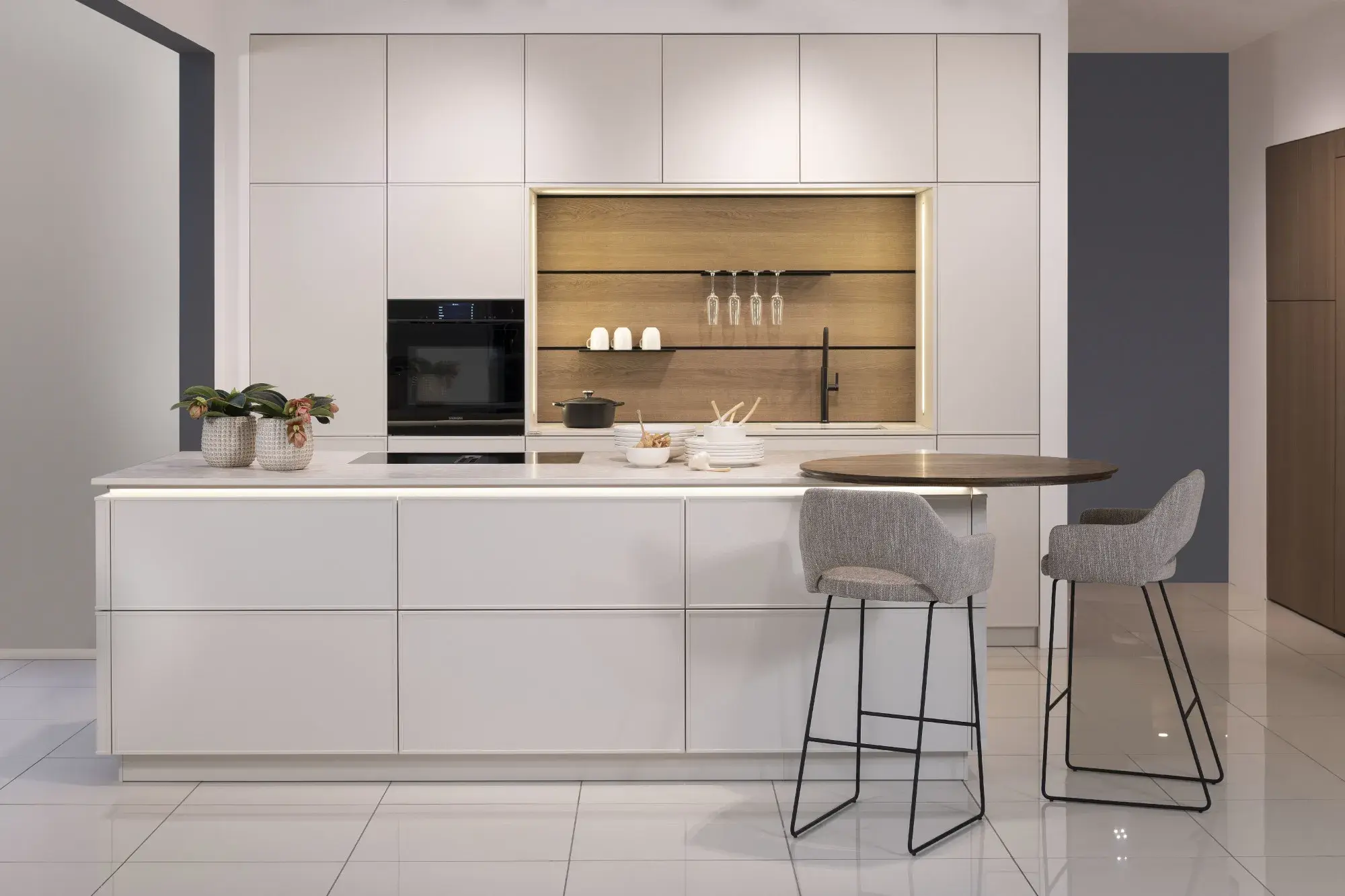 Moderne weiße Küche mit Kochinsel, Hockern und offenem Regal mit Küchenutensilien.