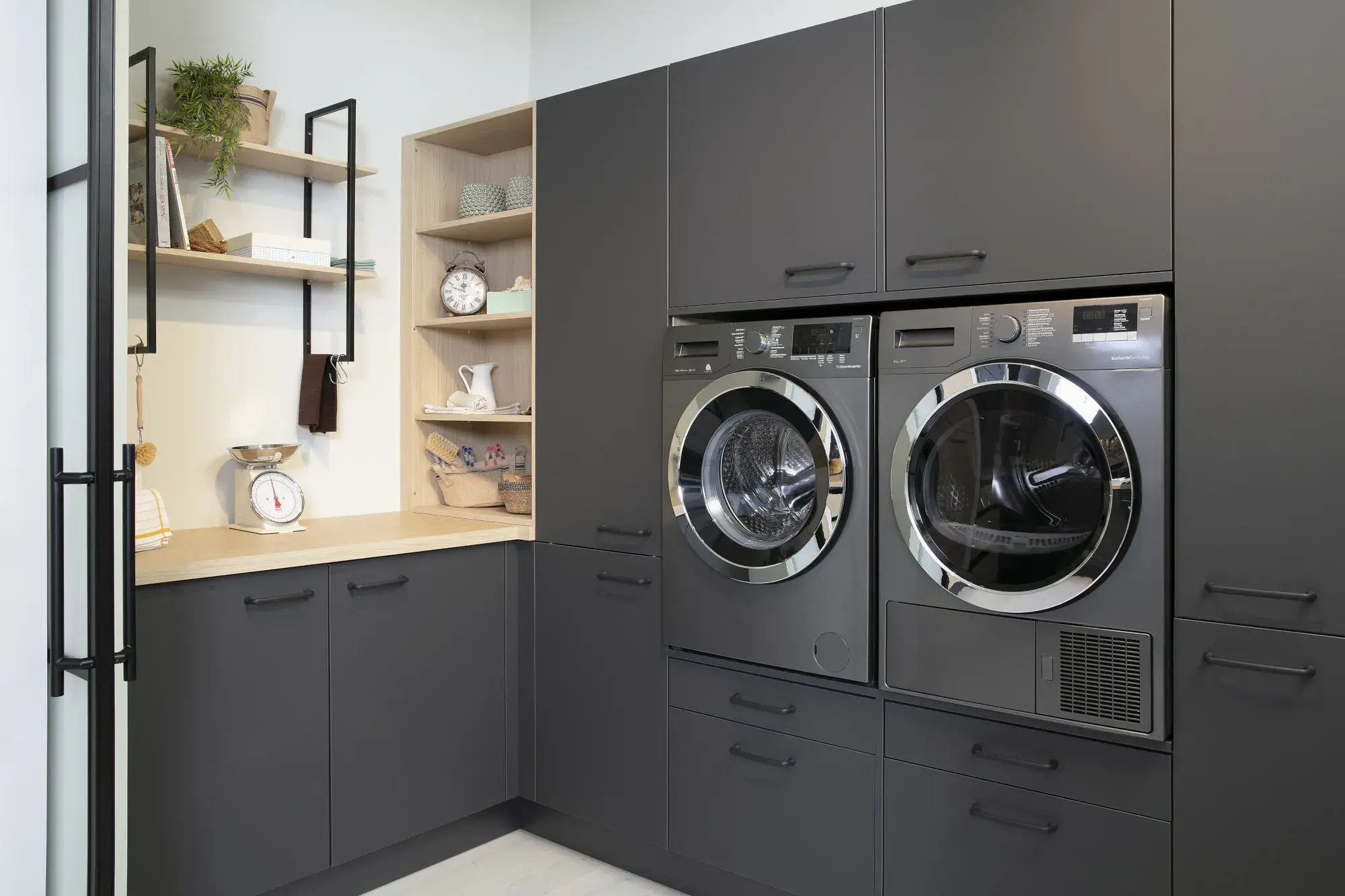 Moderne Waschküche mit schwarzen Schränken, Waschmaschine und Trockner nebeneinander.